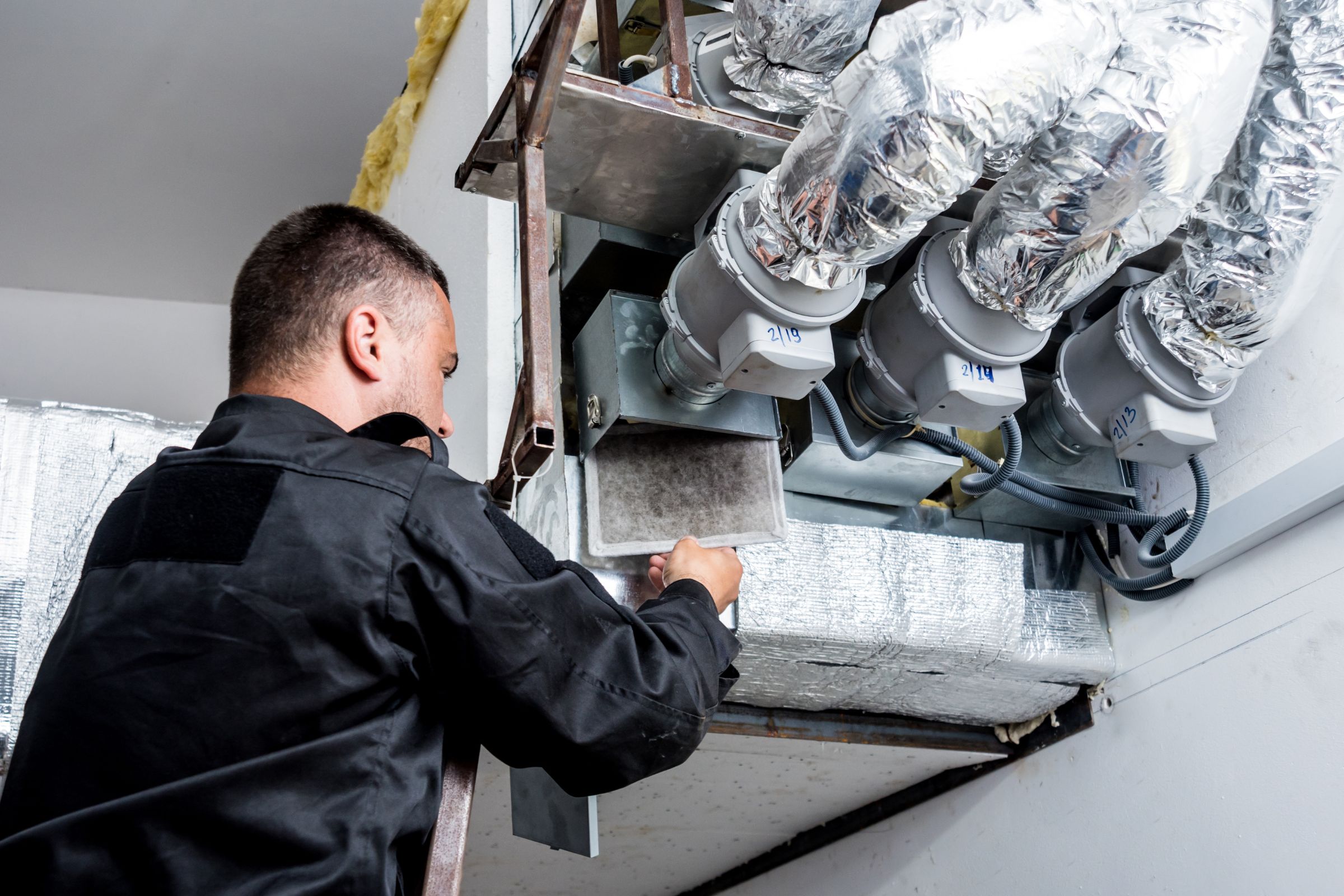 A technician in a black shirt is engaged in furnace maintenance for an HVAC mold removal service in Fresno, CA.