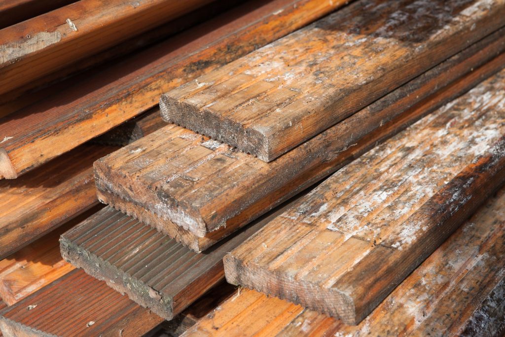 A stack of wood planks showing peeling paint, representing a wood mold removal service in Fresno, CA.